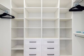 Un placard blanc avec plusieurs étagères et tiroirs, une tringle à vêtements et une petite étagère sur laquelle se trouve une bouteille.