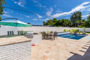 Un patio trasero con piscina, una parrilla y mobiliario exterior.