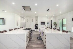Une cuisine moderne dotée d’un îlot central, de meubles blancs et d’un coin repas avec une longue table.