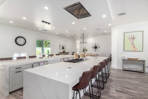 A modern kitchen with a large island, bar stools, and a clock on the wall.