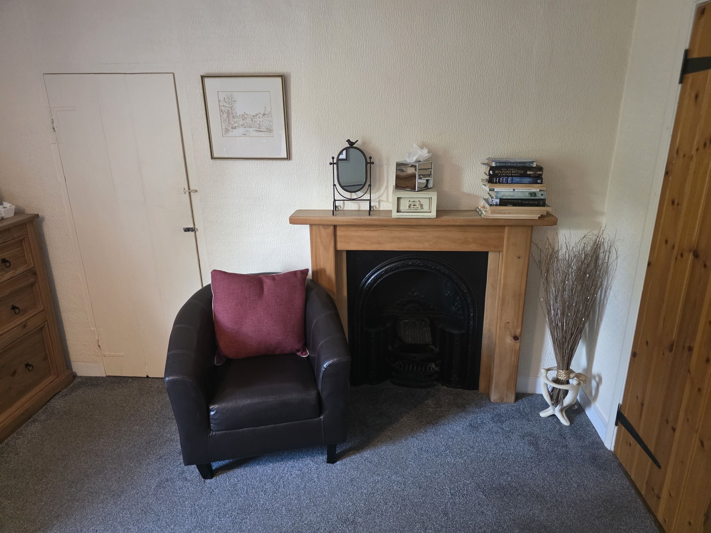 A cozy room with a fireplace, a chair, a wooden dresser, and a shelf with books and decorative items.