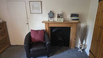 A cozy room with a fireplace, a chair, a wooden dresser, and a shelf with books and decorative items.