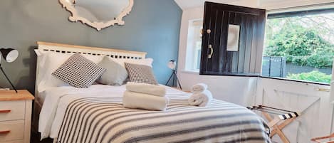 A bedroom with a bed, bedside lamps, a mirror, a chandelier, and a window with a view of greenery.