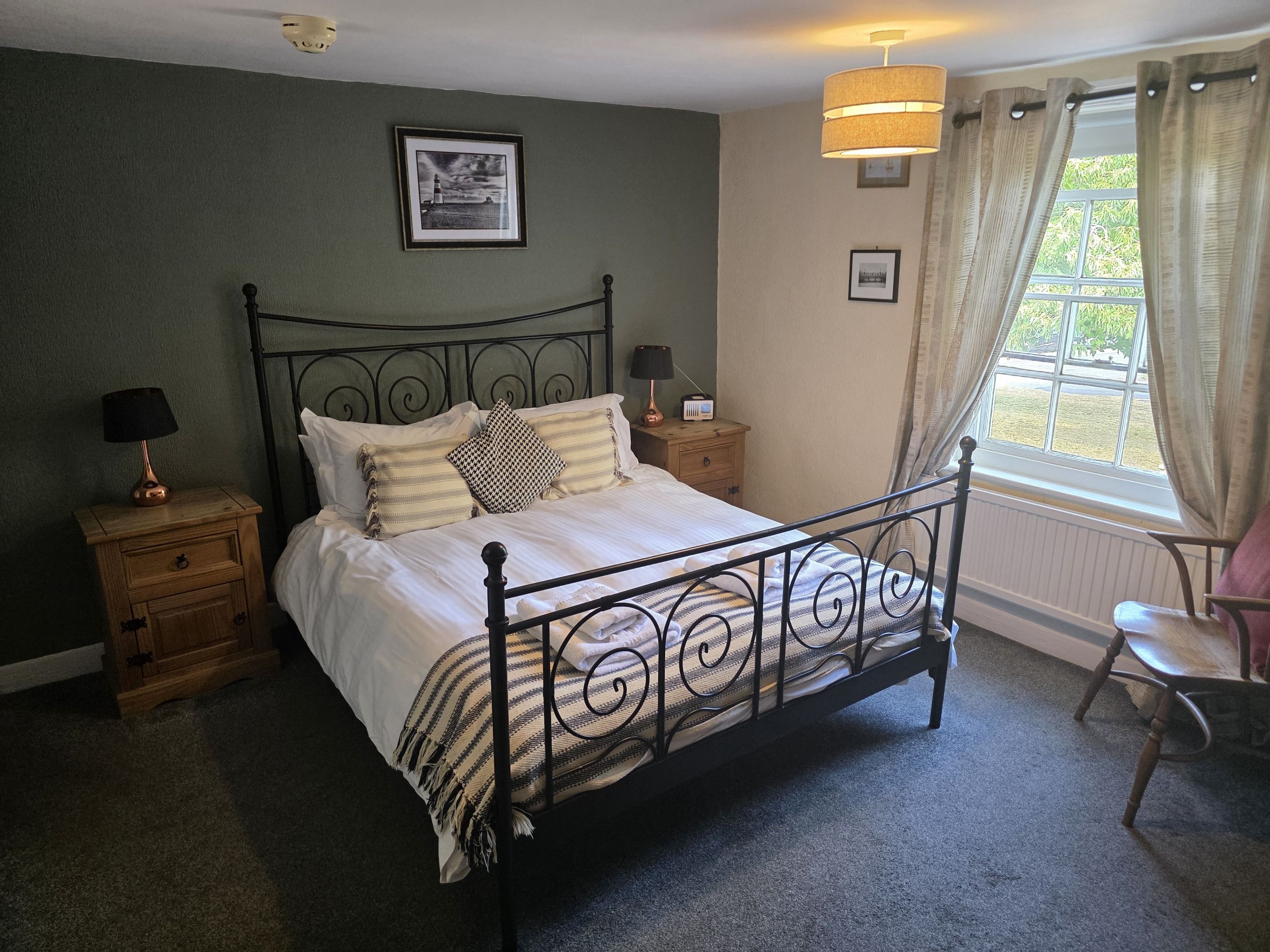A neatly made bed with a metal frame, two bedside tables with lamps, a framed picture on the wall, and a window with curtains.