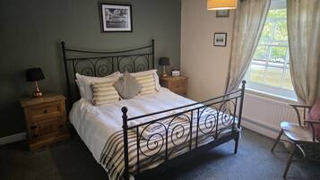 A neatly made bed with a metal frame, two bedside tables with lamps, a framed picture on the wall, and a window with curtains.