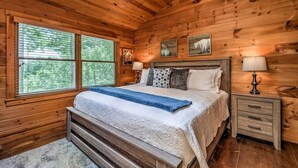 Une chambre dans une cabane en bois, avec un lit, deux tables de chevet et une fenêtre avec des stores.