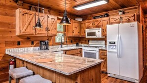 Une cuisine rustique, située dans une cabane en bois, avec un îlot central, un four à micro-ondes, un réfrigérateur et des armoires en bois.