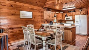 Une cuisine aménagée dans le style d’un chalet en bois, avec une table à manger, des chaises et un réfrigérateur.