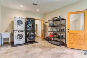 A laundry room with stacked washers and dryers, a small table, and a shelf with cleaning supplies.