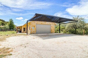 A single-story building with a covered garage and a gravel driveway. - Roadrunner | Riverfront 3BR with Views & Fire Pit (Leakey)