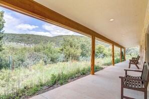 A covered outdoor area with wooden beams, a concrete floor, and a view of a hilly landscape.