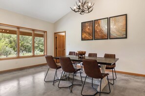 A dining room with a large table, six chairs, and three framed artworks on the wall.