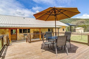 An outdoor deck with a table and chairs, a large umbrella, and a stone building in the background.