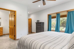 A bedroom with a bed, a dresser, a wardrobe, and a window with curtains. - Roadrunner | Riverfront 3BR with Views & Fire Pit (Leakey)