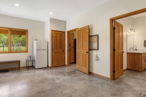 A hallway with wooden doors, a refrigerator, a bench, and a window with a view of greenery.