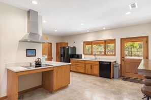 A modern kitchen with a central island, wooden cabinets, stainless steel appliances, and a window providing a view of the outdoors.