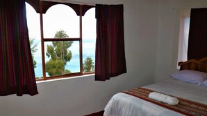 Una habitación con cama, ventana con cortinas y vista al mar.