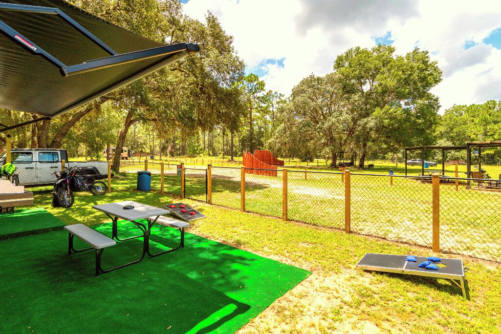 A fenced outdoor area with picnic tables and a tennis court.