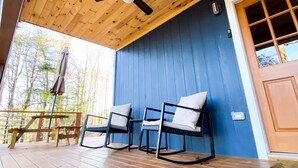 A wooden deck with a ceiling fan, two rocking chairs, a table, and a door with windows. - Charming Cottage Near Downtown, Parkway, and Biltmore (Asheville)