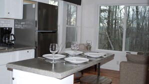 A modern kitchen with a central island, white cabinets, and a large window offering a view of trees. - Charming Cottage Near Downtown, Parkway, and Biltmore (Asheville)