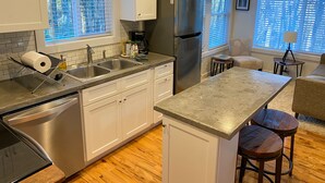 A modern kitchen with stainless steel appliances, white cabinetry, and a large island with stools. - Charming Cottage Near Downtown, Parkway, and Biltmore (Asheville)