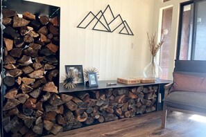 Uma sala de estar com lareira, um painel de madeira com lenha e uma obra de arte moderna.