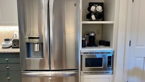 Ein Edelstahl-Kühlschrank mit Wasserspender, Mikrowelle und Kaffeemaschine auf der Arbeitsfläche.