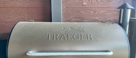 A Traeger grill with a handle and a logo, set against a wooden wall.