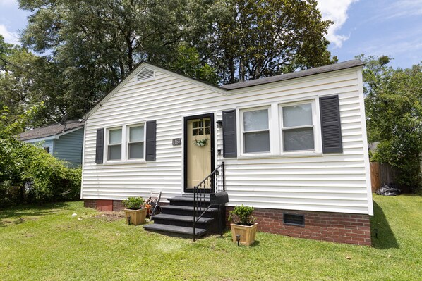 A single-story house with a front porch, a small front yard, and a brick foundation.
