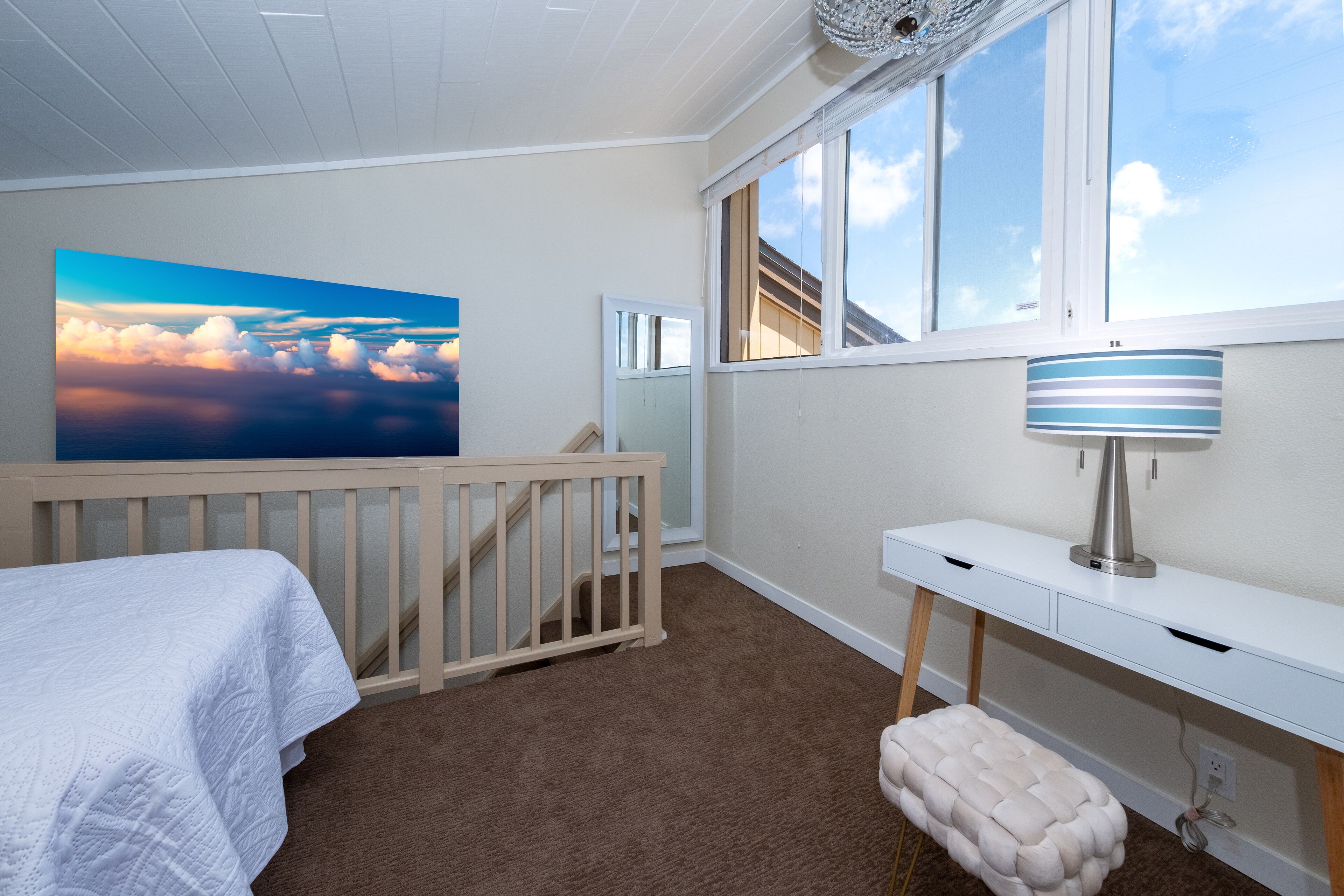 Ein Schlafzimmer mit Babybett, Schreibtisch, Lampe und einem großen Fenster mit Blick auf den Himmel.
