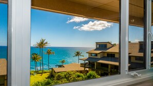 A view from a window overlooking a coastal area with palm trees and a clear sky. - Remodeled Family-Size Condo with Fantastic View of the Ocean and Pool (Koloa)