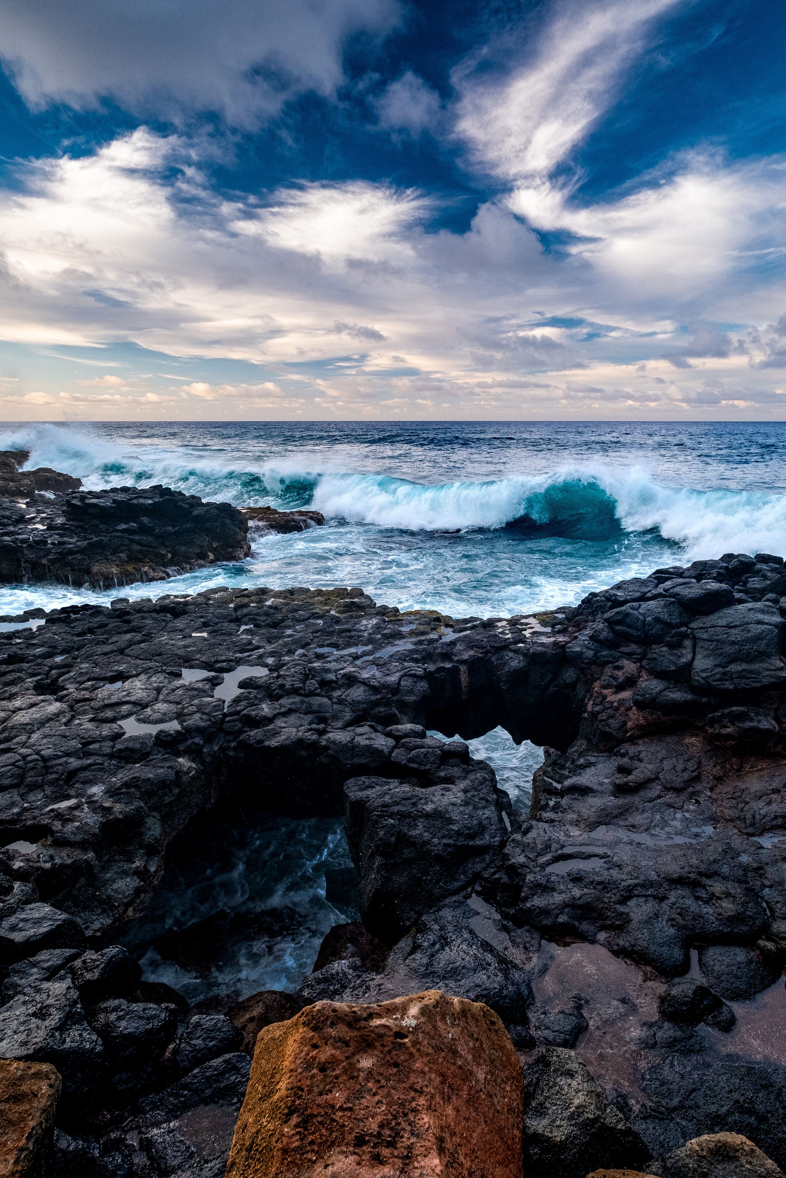 A rocky shoreline with waves crashing against the rocks under a cloudy sky.