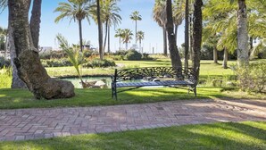A park with a paved walkway, a metal bench, and palm trees.