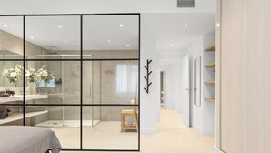 A modern bedroom with a large bed, a glass shower enclosure, and a walk-in closet with shelves.