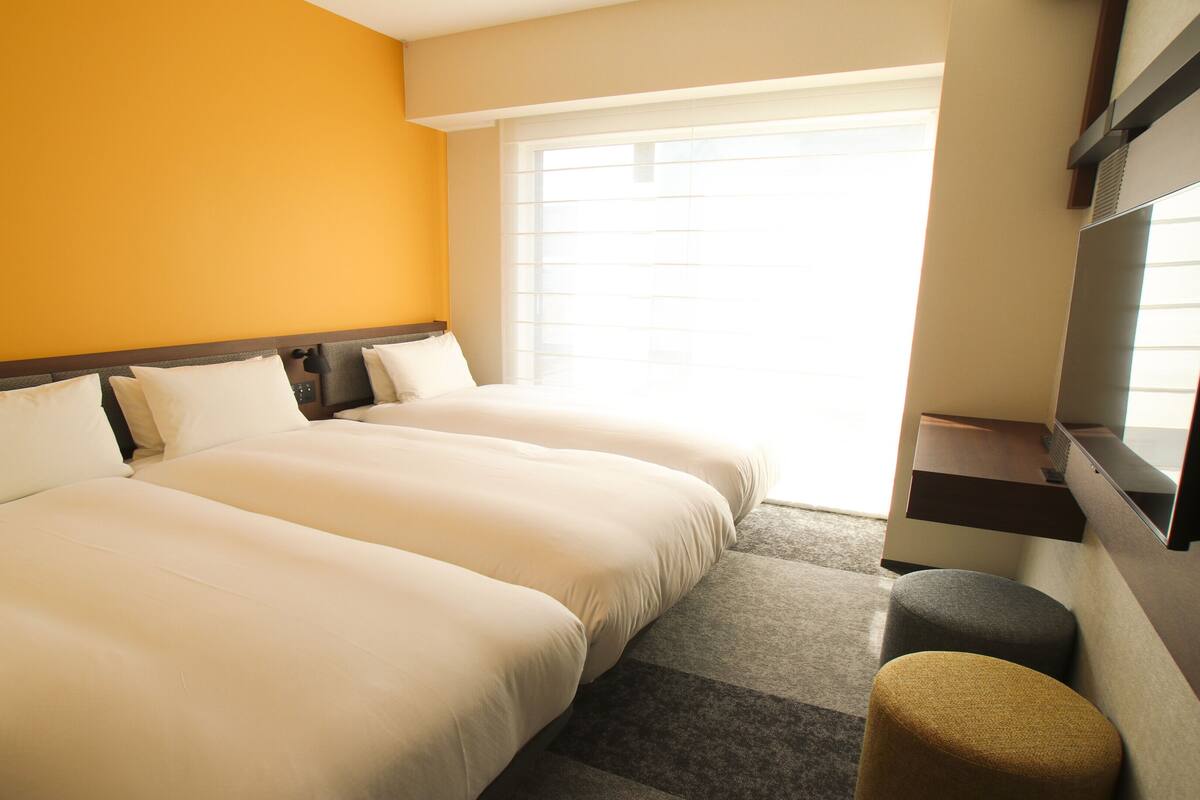 A hotel room with two beds, a TV, and a window.