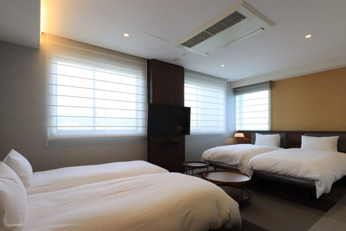A hotel room with two beds, a TV, a lamp, and a window with blinds.
