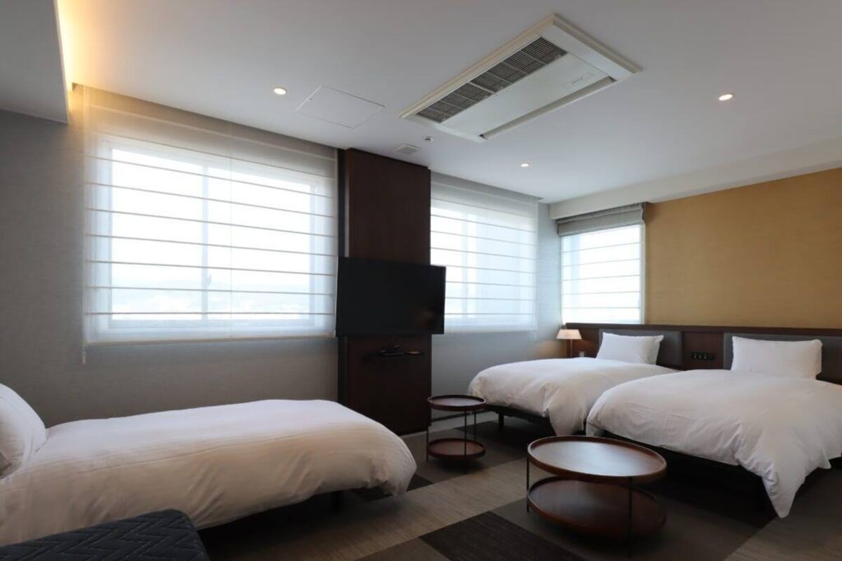 A hotel room with two beds, a TV, a small table, and a window with blinds.