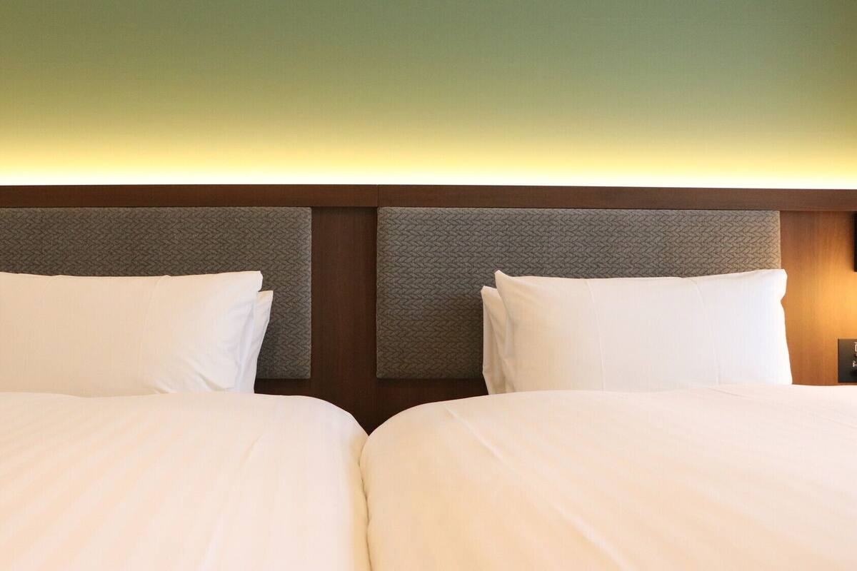 A hotel room with two beds, a wooden headboard, and a wall-mounted light fixture.