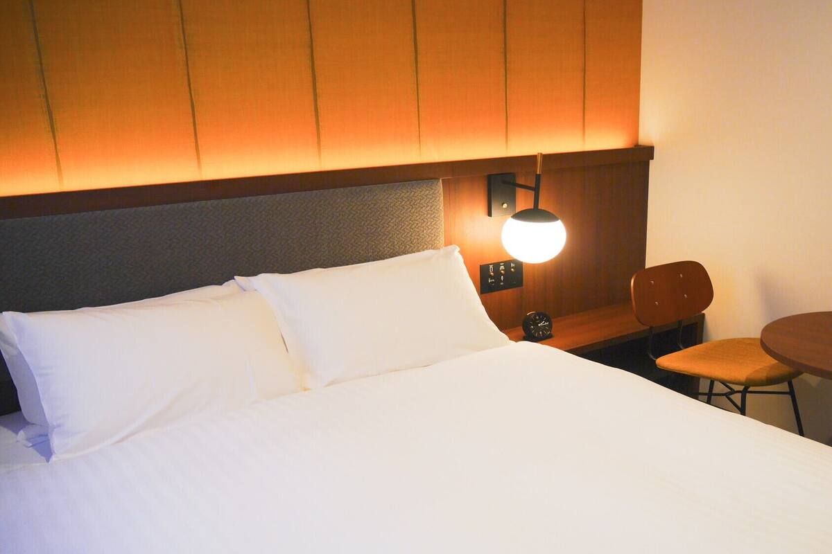 A hotel room with a bed, a nightstand with a lamp, a chair, and a small table.