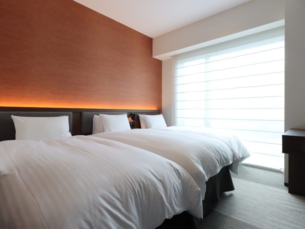 Une chambre d’hôtel avec un grand lit, une tête de lit, une table de chevet et une fenêtre avec des stores.