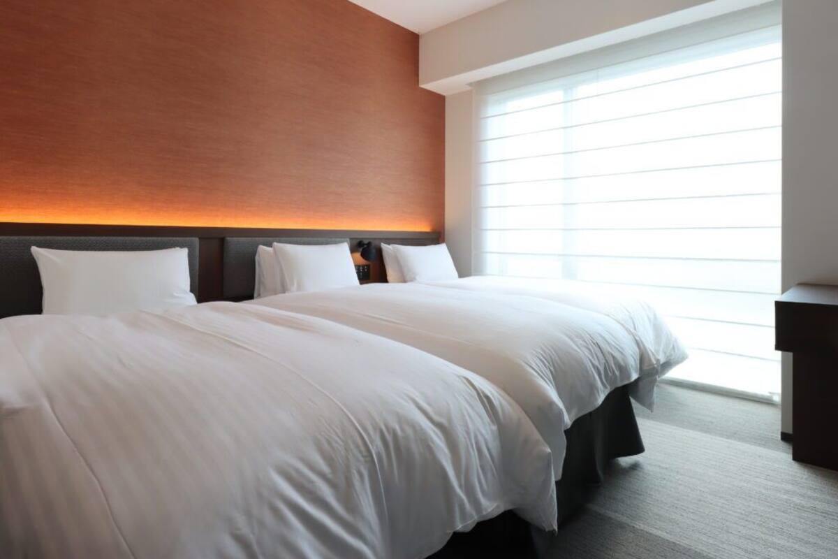 A hotel room with a large bed, a headboard, a bedside table, and a window with blinds.