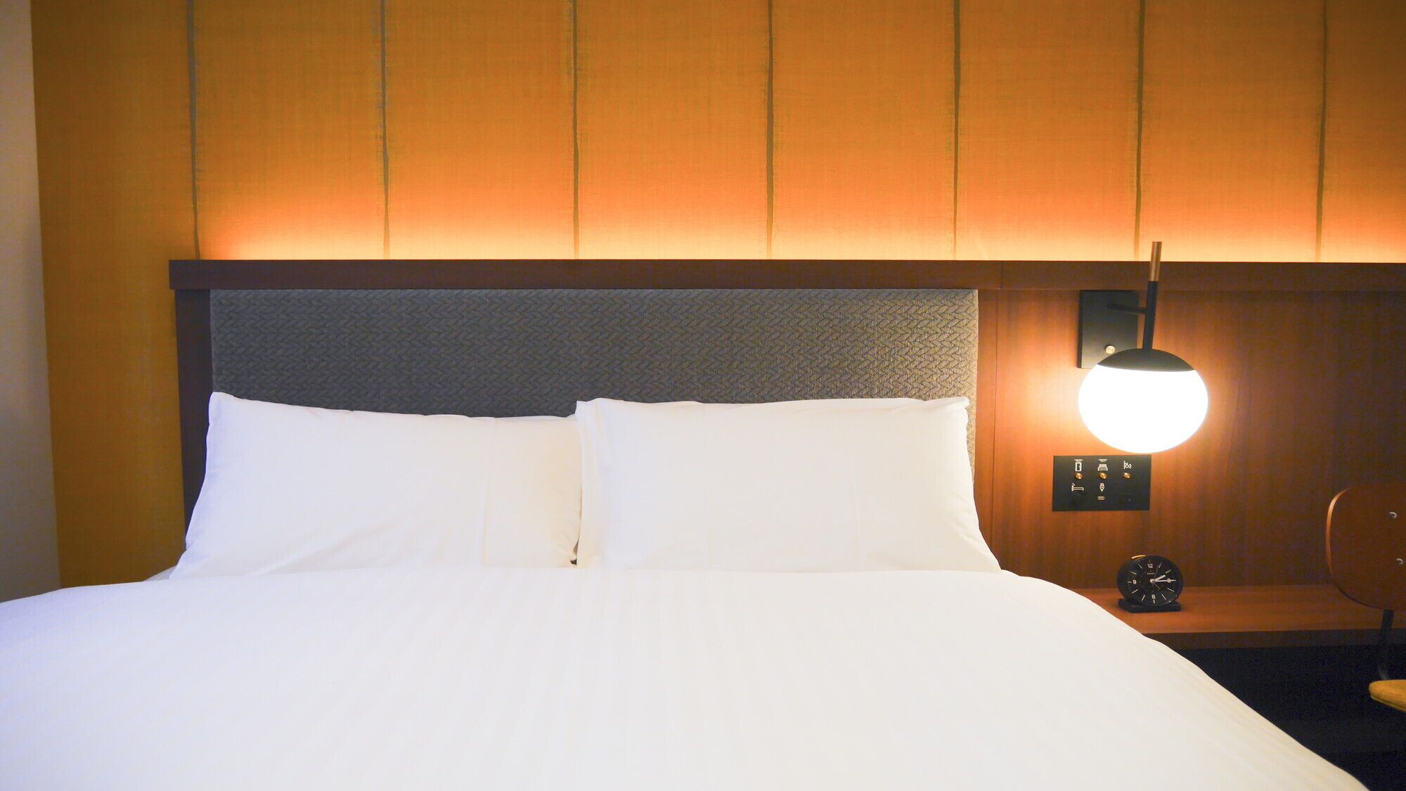 Une chambre d’hôtel avec un lit, une table de chevet avec une horloge et une lampe fixée au mur.