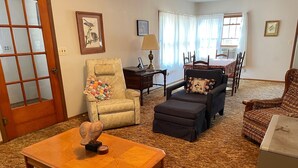 A living room with a wooden coffee table, two armchairs, a sofa, a dining table with chairs, and a window with curtains. - Unplug and enjoy outdoor living at the Lazy Easy (Pet-friendly!) (Bassett)