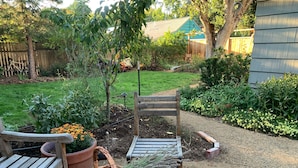 A wooden bench and a wicker basket with lavender in a garden area with a wooden fence and a house in the background.