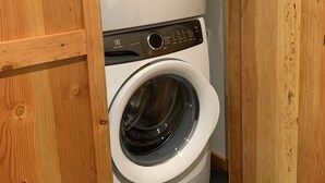 A compact laundry room with a front-loading washer and dryer, wooden paneling, and black tiled flooring.