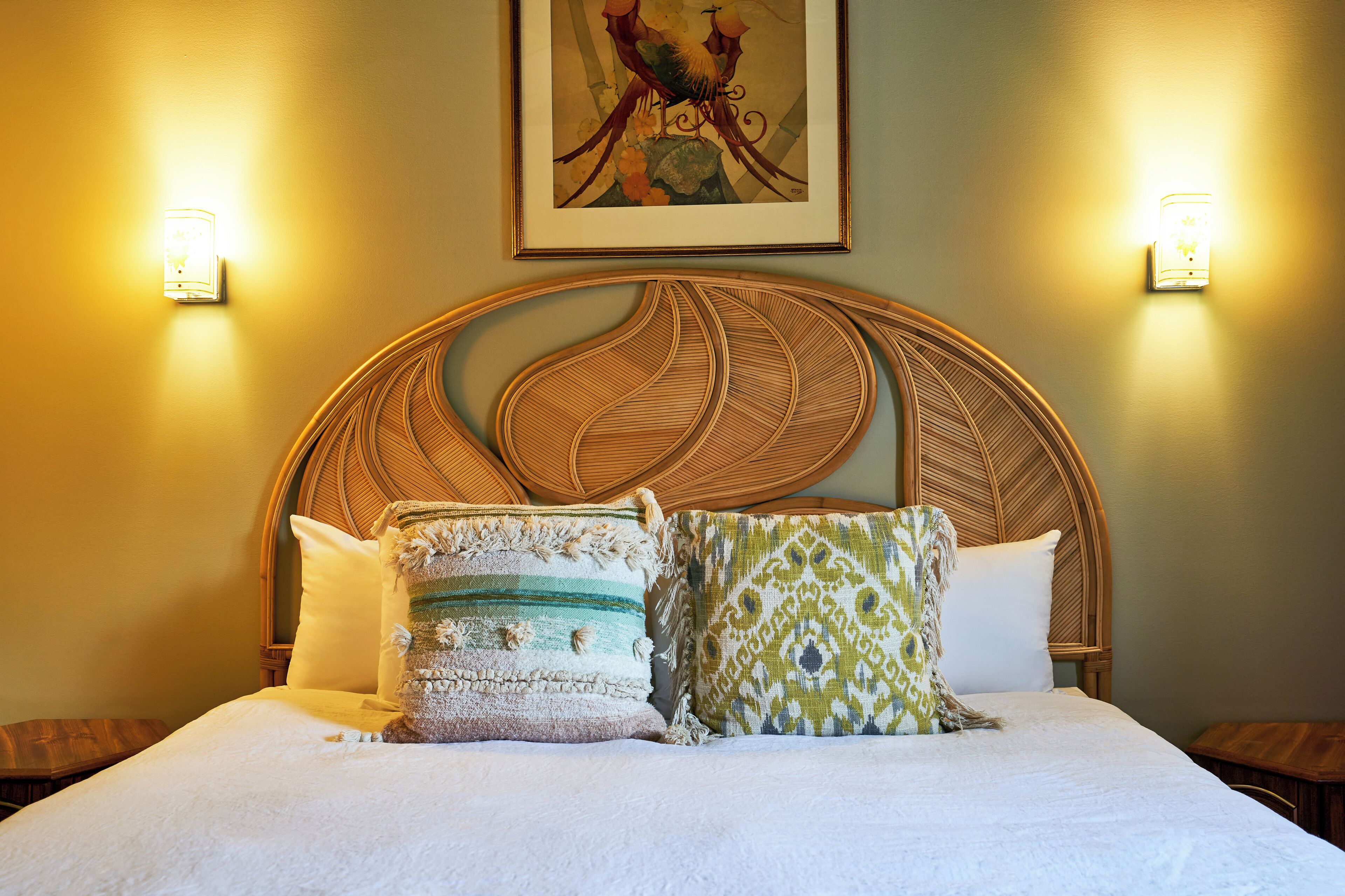 A bed with a woven headboard, two wall-mounted lights, and a framed artwork above.