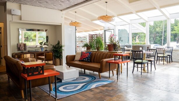 A spacious indoor area with a brown leather sofa, a coffee table, and a dining table with chairs. There are potted plants and a large window providing natural light. - Motel Chelsea (Chelsea)