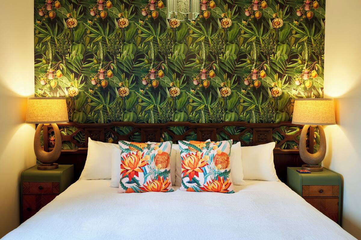 Ein Hotelzimmer mit einem Bett, zwei Nachttischen, zwei Lampen und floralem Wandpapier.