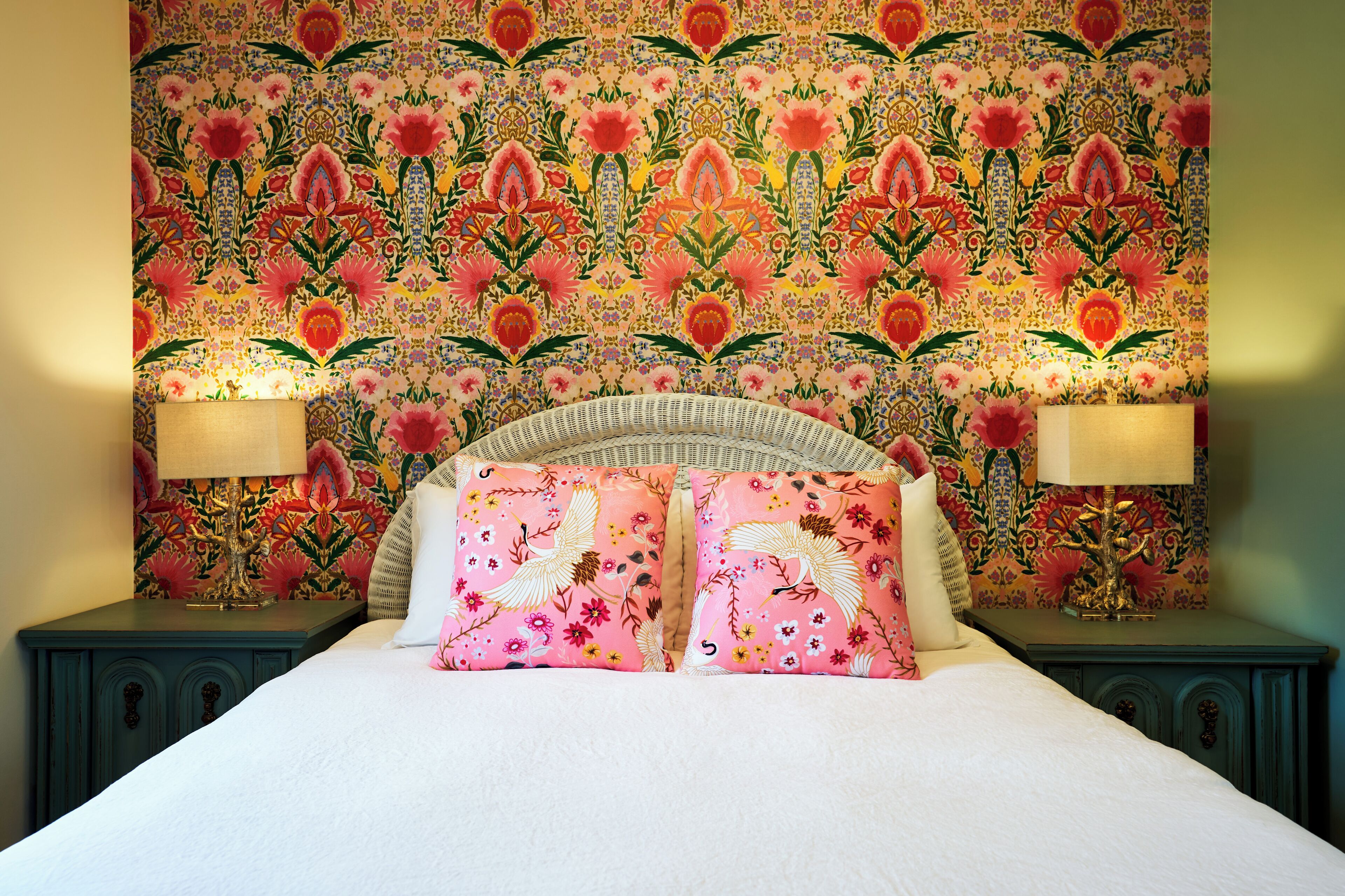 Un lit avec une tête de lit ornée d’un motif floral, deux lampes de chevet et un mur recouvert d’un papier peint floral aux motifs détaillés.