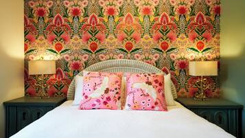 Un lit avec une tête de lit ornée d’un motif floral, deux lampes de chevet et un mur recouvert d’un papier peint floral aux motifs détaillés.